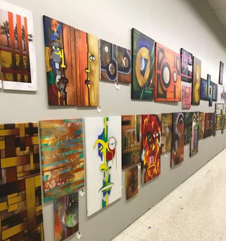 A wall of artwork, abstract shapes mostly in yellow and orange.